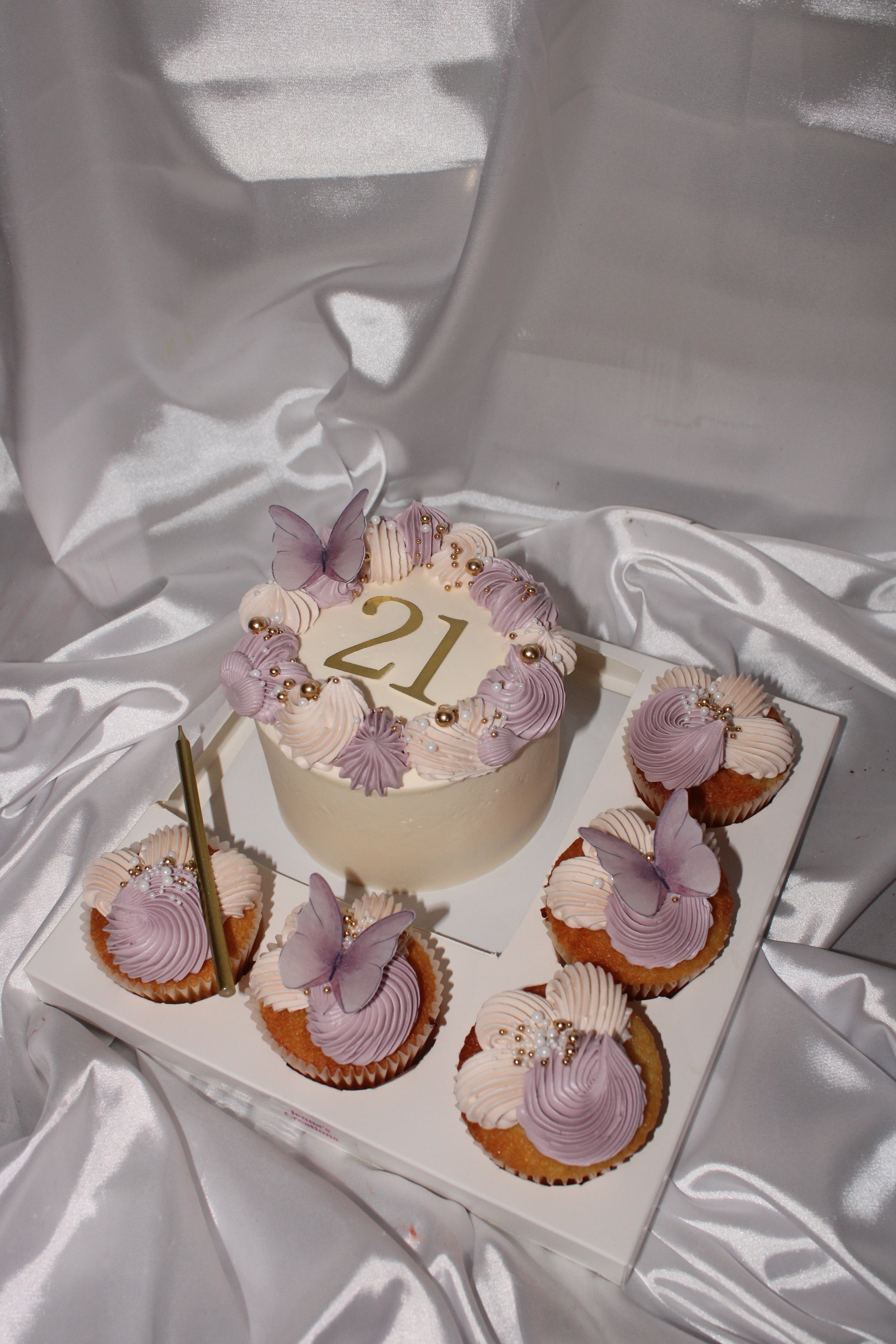 Decorative cake with number 21 and matching cupcakes on a white fabric background