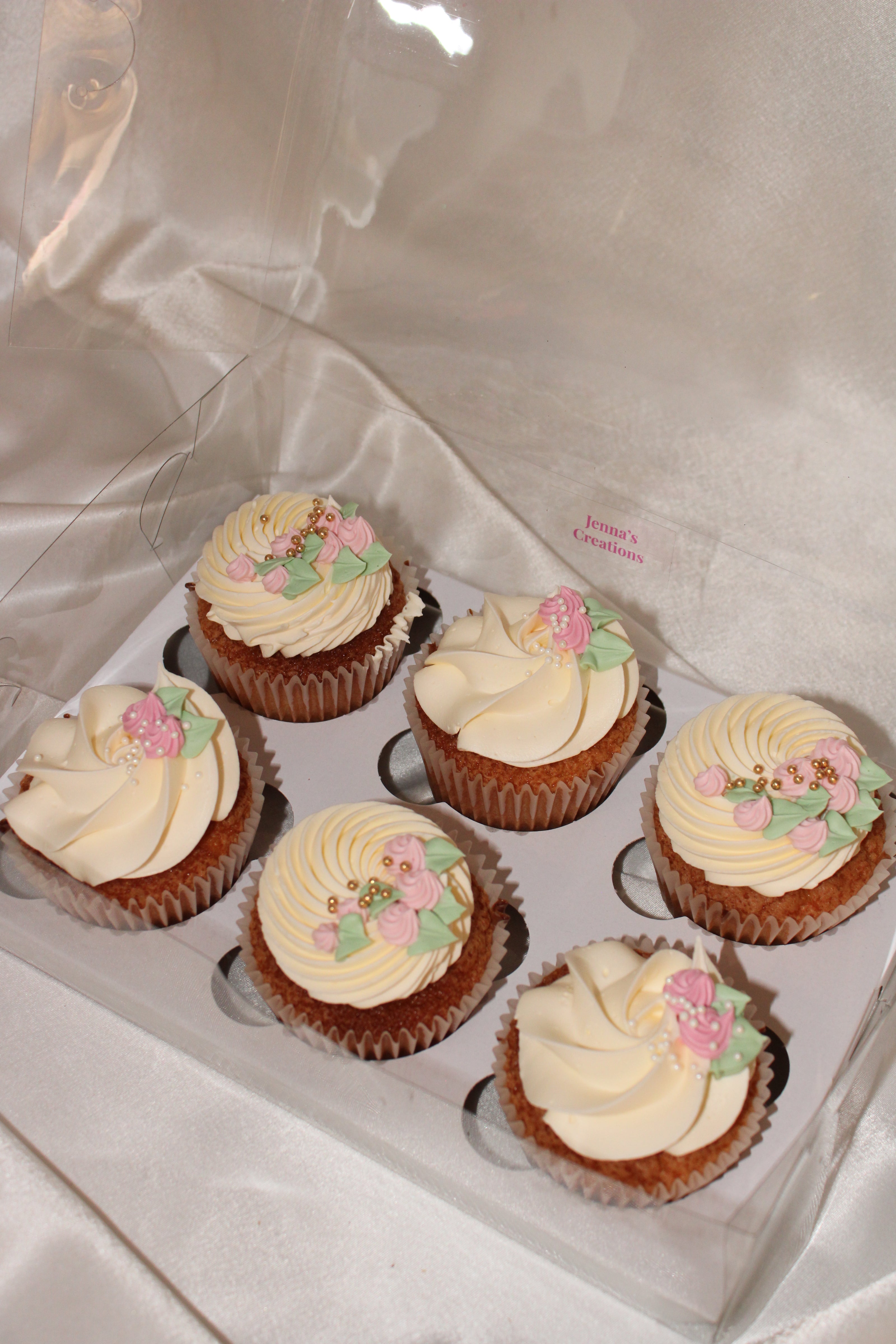 Decorative cupcakes with floral designs in a clear box on a white background