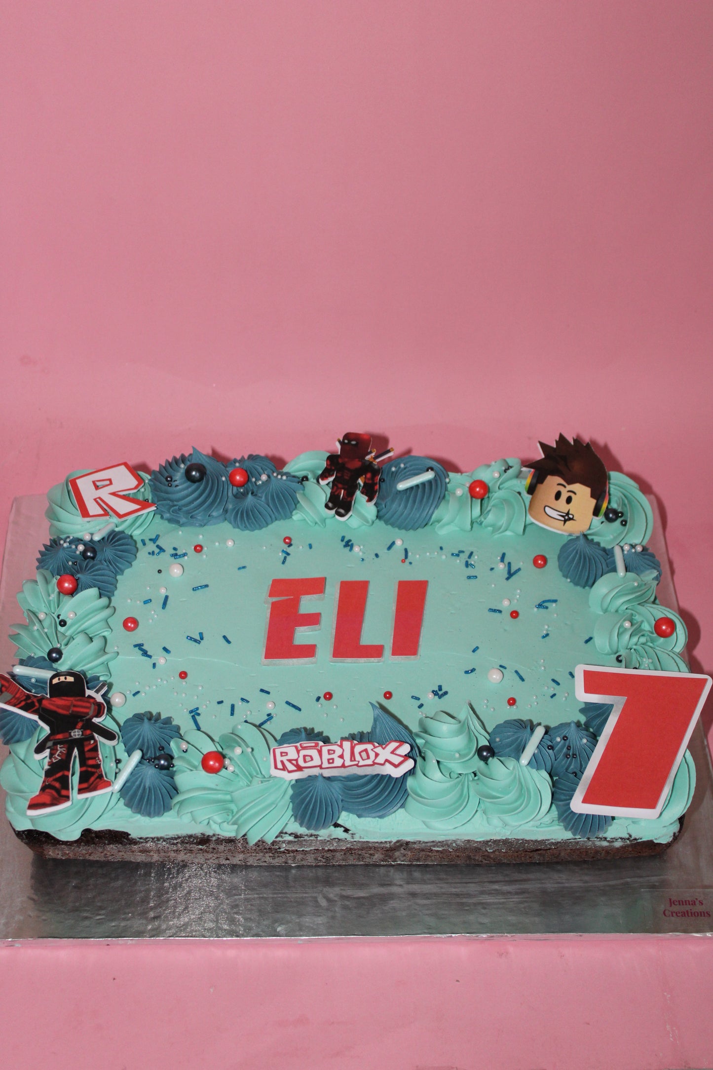 Decorative cake with blue frosting, red letters, and cartoon character on a pink background