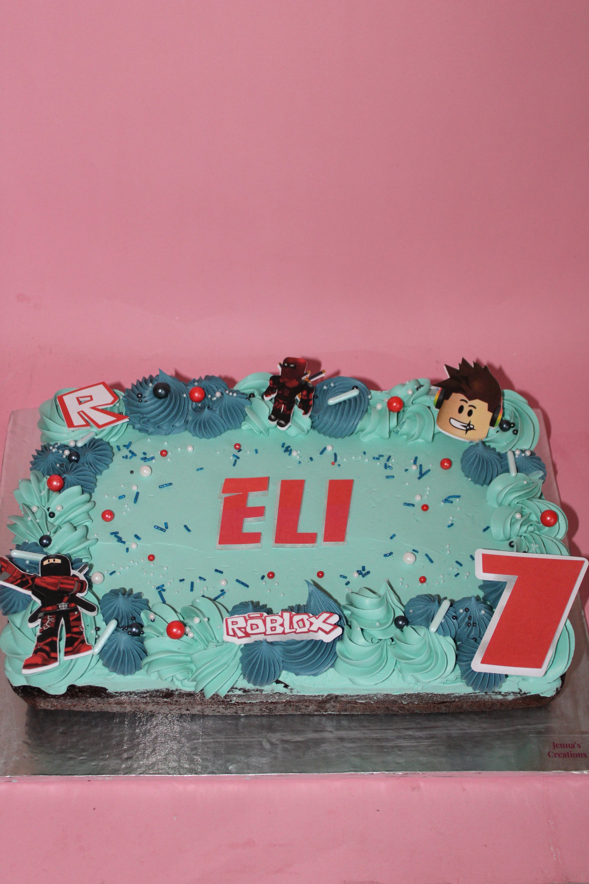 Decorative cake with blue frosting, red letters, and cartoon character on a pink background