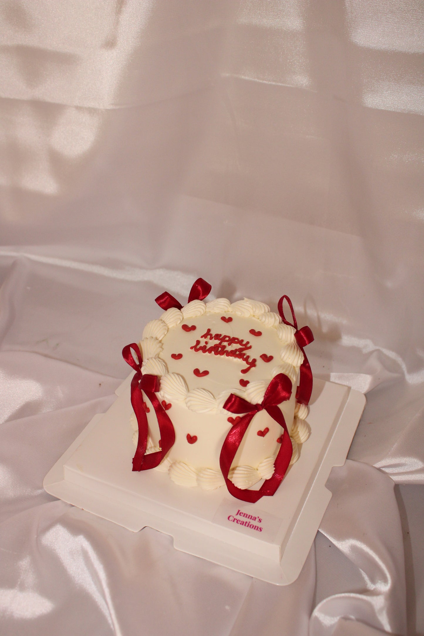 Small white cake with red ribbons on a white plate against a white background