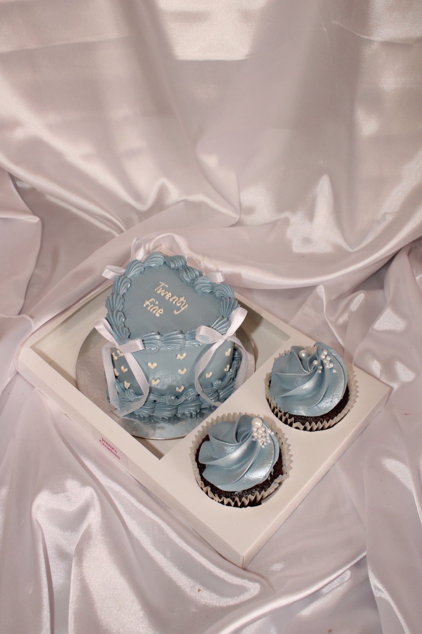 Decorative blue cupcakes in a box on a satin surface