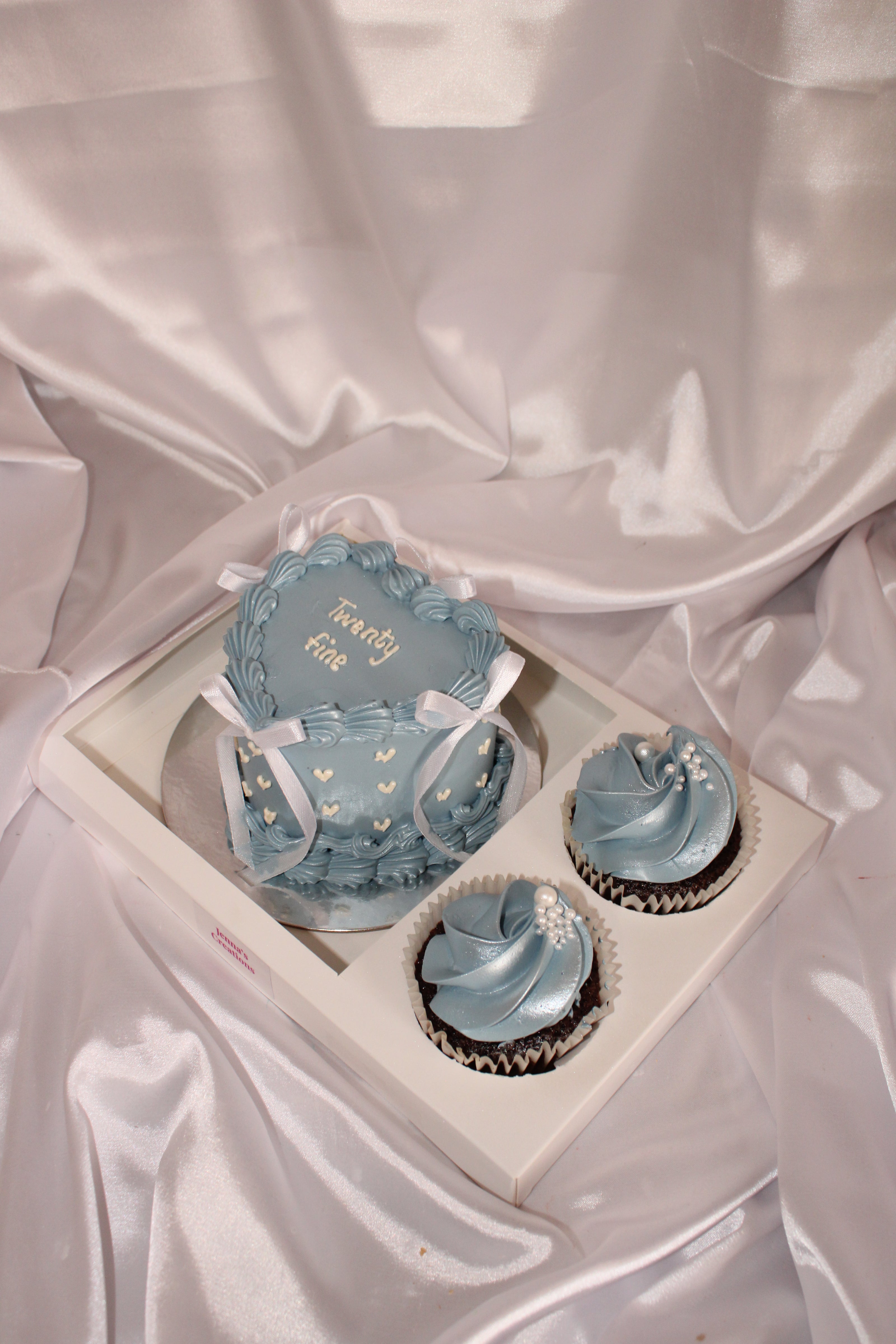 Decorative blue cupcakes in a box on a satin surface