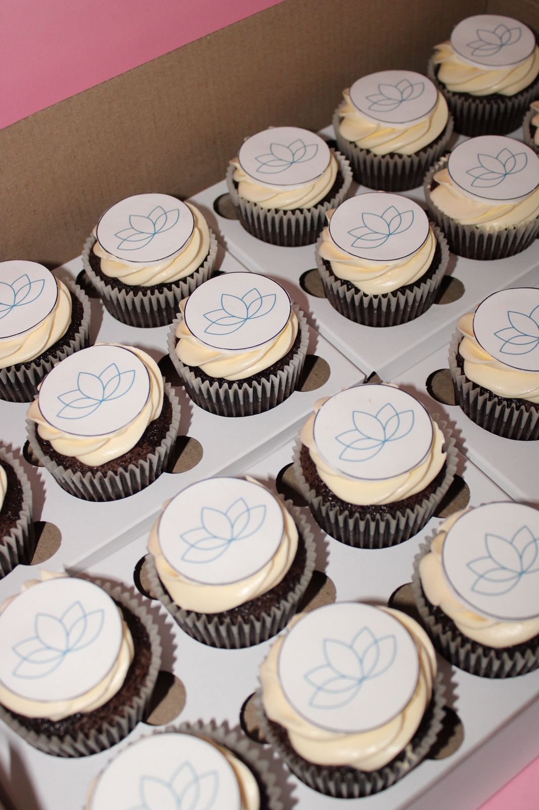 assorted cupcakes with smooth frosting and edible branded logo toppers presented on a clean, professional display tray.