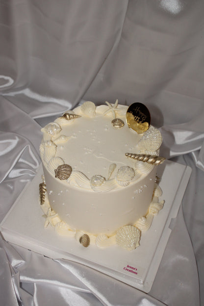 Round celebration cake with coastal-inspired design, including starfish and seashell decorations with subtle shimmer.