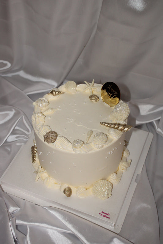 Round celebration cake with coastal-inspired design, including starfish and seashell decorations with subtle shimmer.