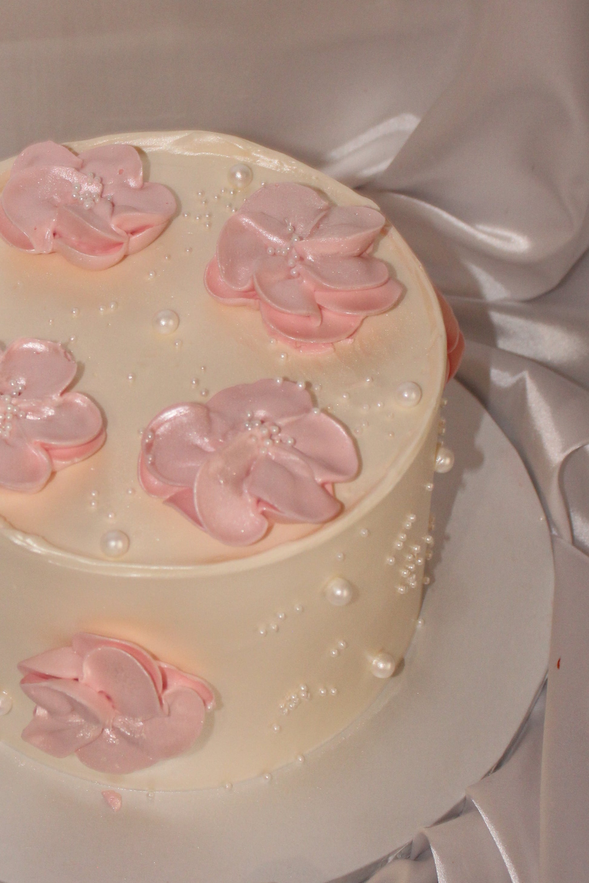 Vintage-style round cake with blush pink blossoms and scattered edible pearls on smooth white frosting.