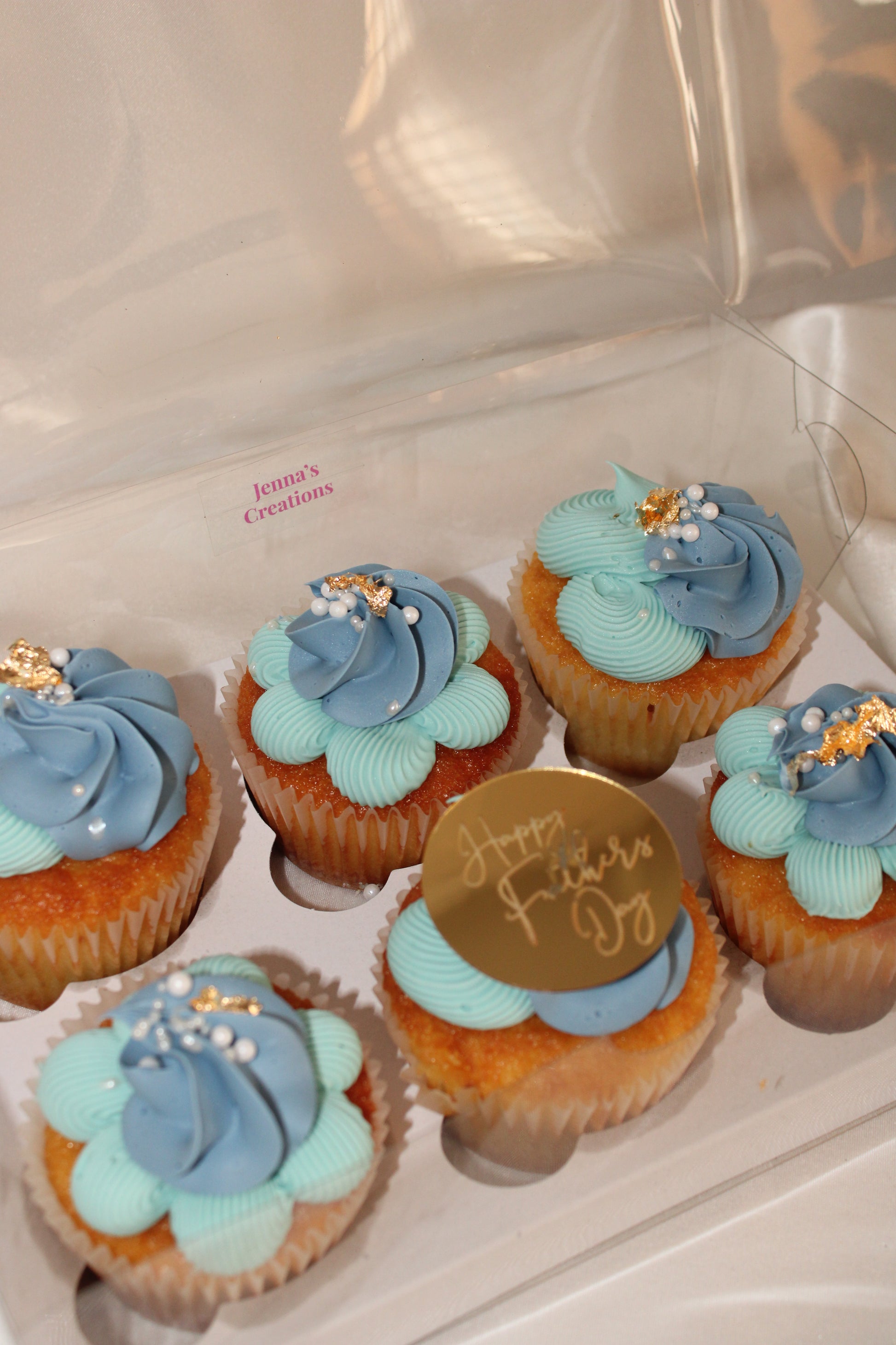 Elegant Father’s Day cupcake gift box featuring blue frosting and gold accents in a clear presentation box.