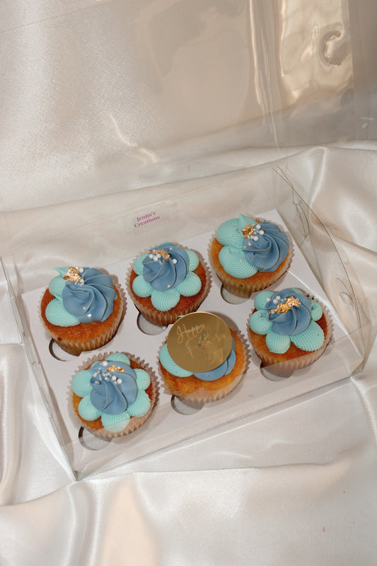 Box of six Father’s Day cupcakes decorated with blue buttercream swirls, gold leaf, and white sugar pearls.