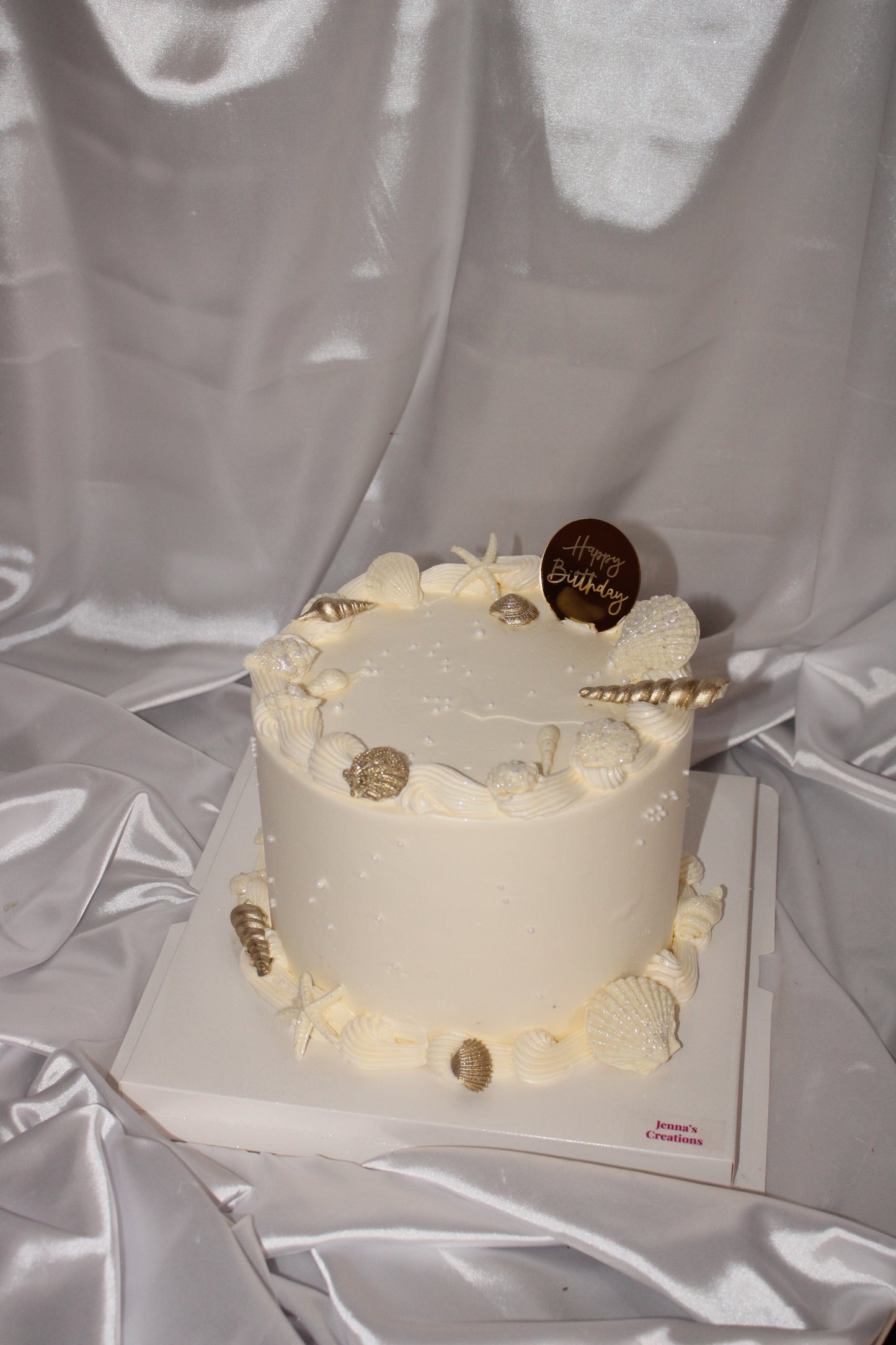 Elegant ocean-themed cake featuring textured piping and handcrafted shells in white and gold tones.