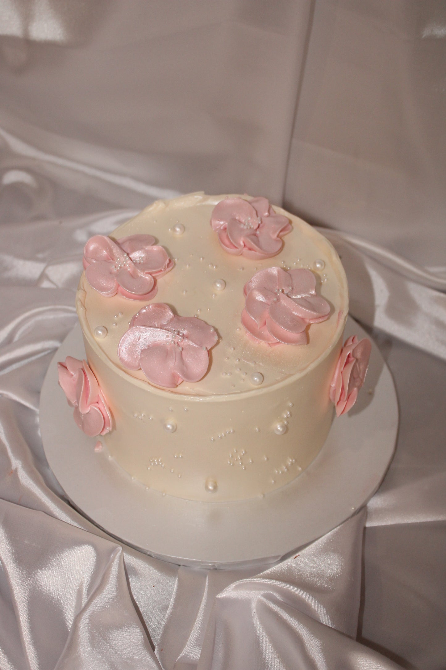 Minimalist celebration cake featuring delicate pink flowers and pearl embellishments on a creamy buttercream finish.