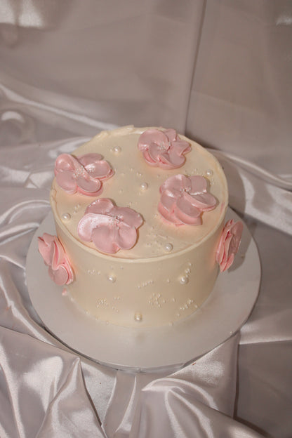 Minimalist celebration cake featuring delicate pink flowers and pearl embellishments on a creamy buttercream finish.
