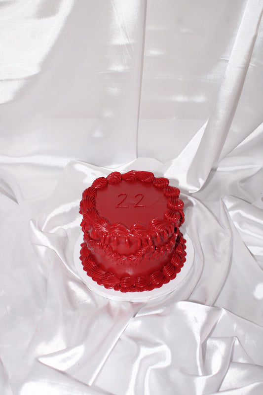 “Red vintage-style heart cake with the number 22 on top, placed on white satin fabric backdrop.”