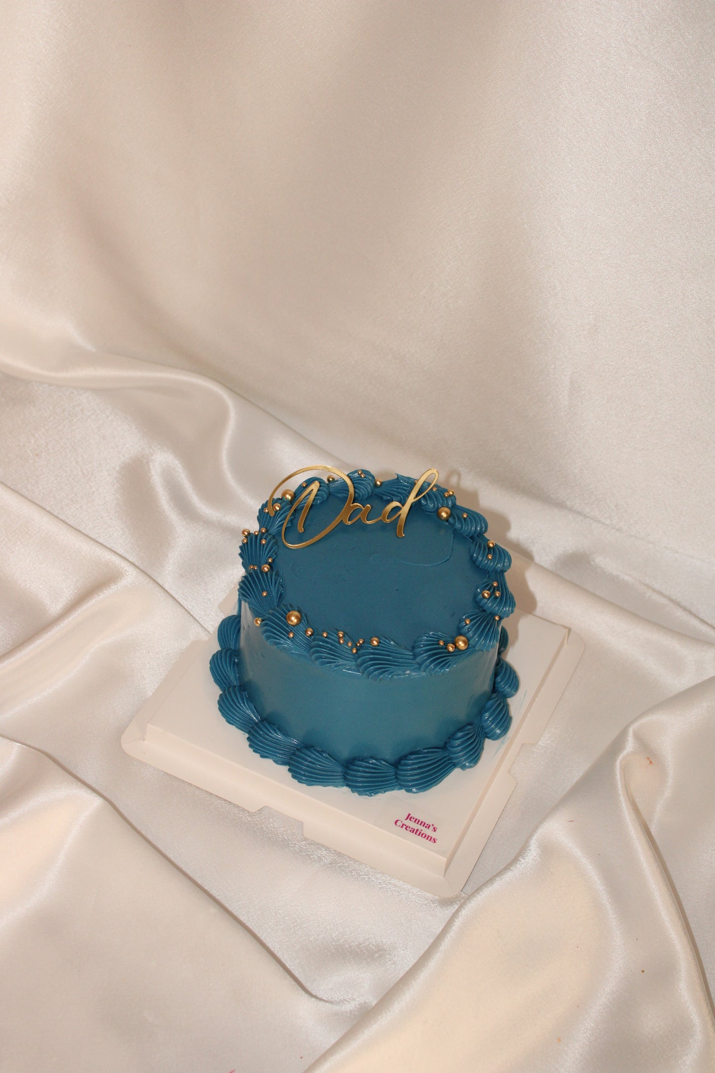 Modern Father’s Day cake in royal blue frosting with decorative gold accents and script Dad topper.