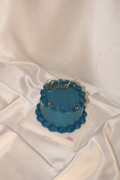 Modern Father’s Day cake in royal blue frosting with decorative gold accents and script Dad topper.